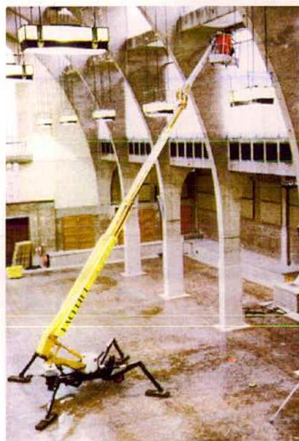 Interior photograph of a large building under construction featuring concrete arches and a yellow cherry picker.
