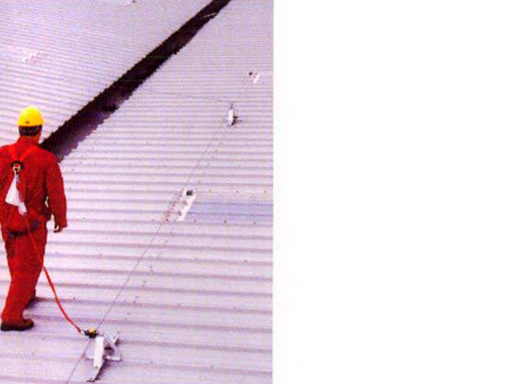 A photograph showing a construction worker in red overalls and a yellow hard hat walking on a large corrugated metal roof.