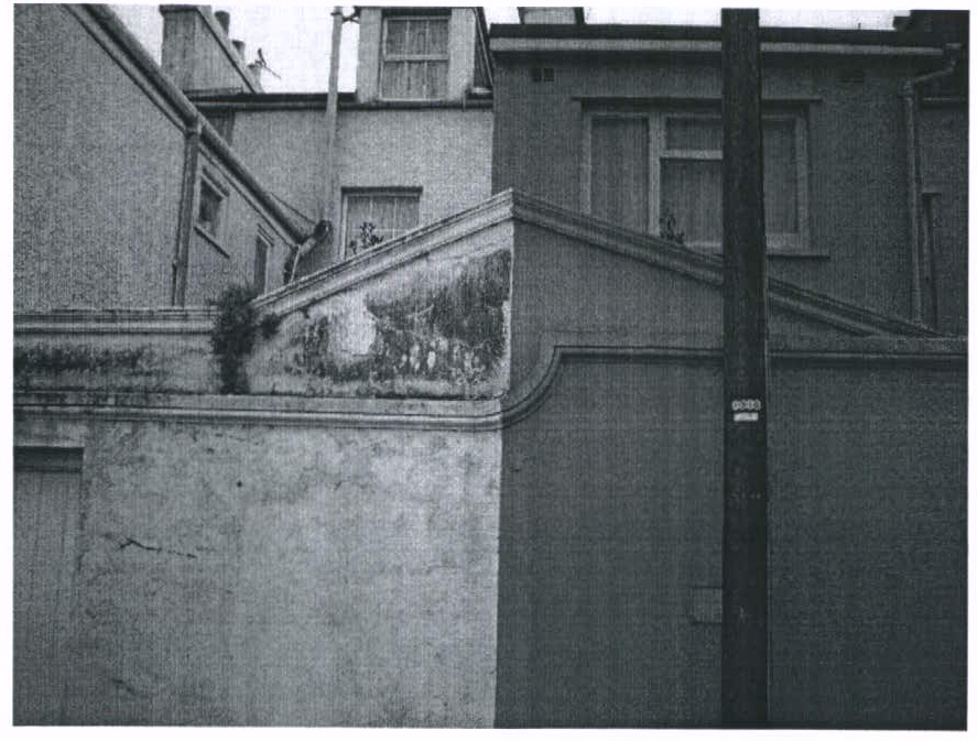 A black and white photograph showing the rear elevation of a residential property with a low boundary wall and upper-story windows.