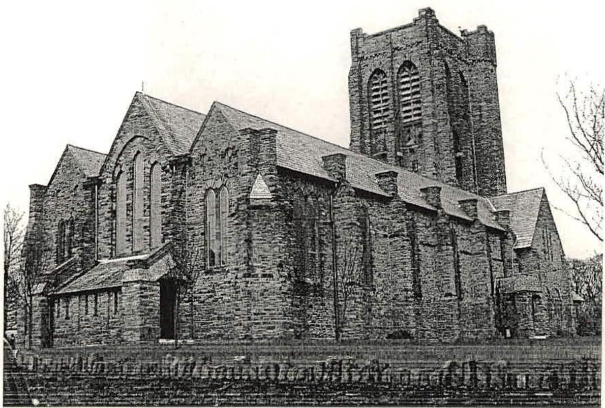 A black and white photograph of a large stone church building featuring a prominent tower and arched windows.
