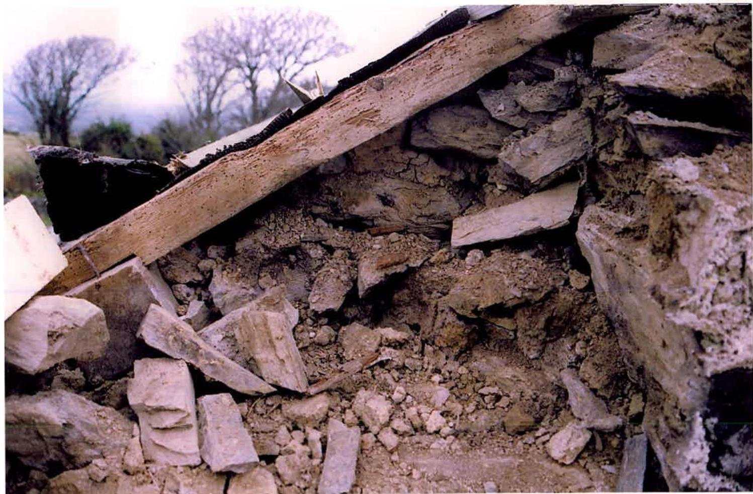 A close-up photograph showing the interior of a collapsed stone structure with exposed wooden beams and rubble.