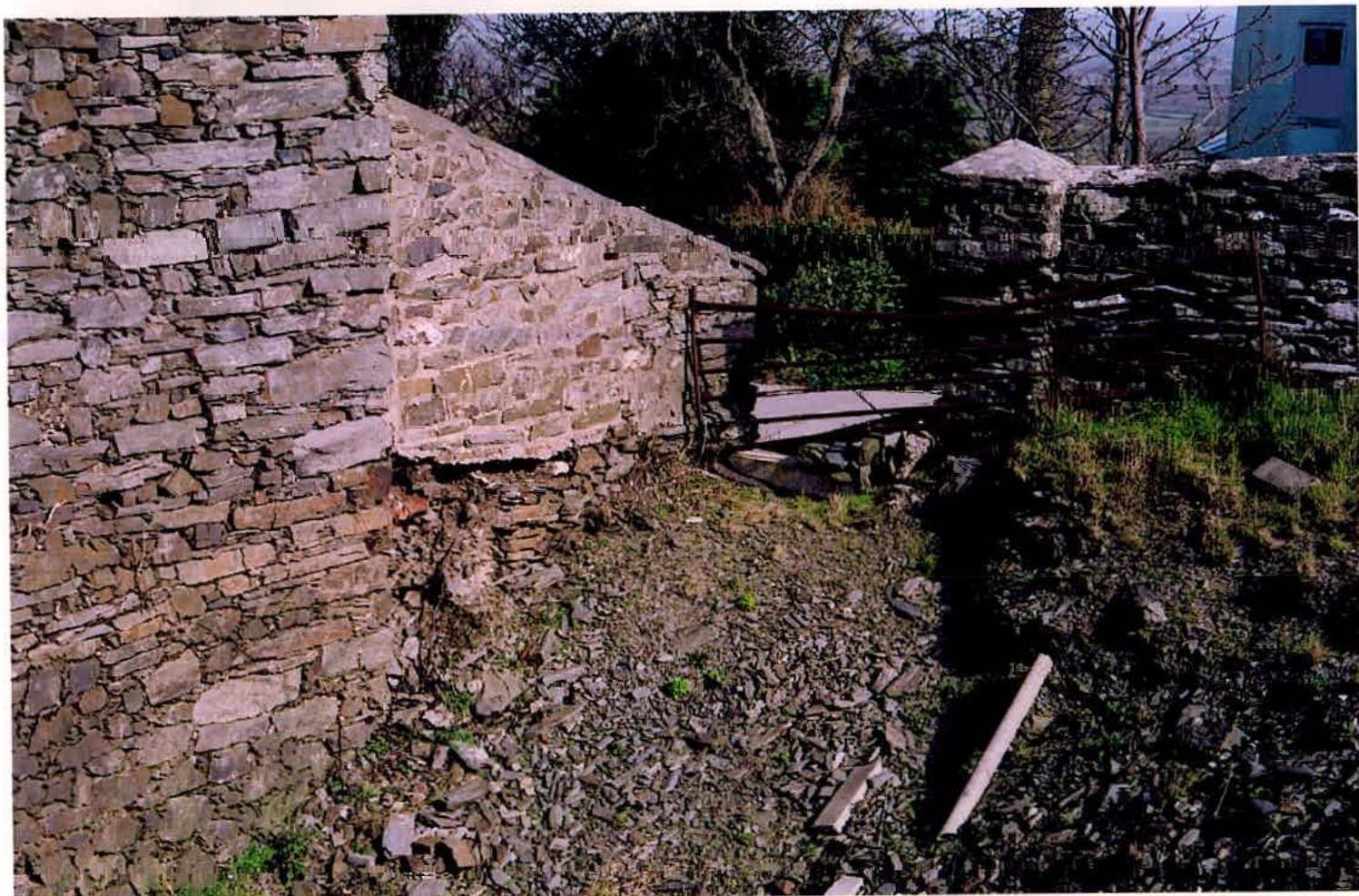 A photograph showing a weathered stone wall and ground covered in rubble, indicating demolition or renovation work on a rural structure.