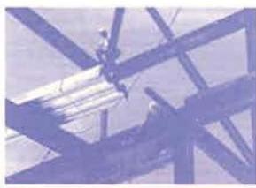A photograph showing the exposed roof truss structure of a building under construction with workers visible on the beams.