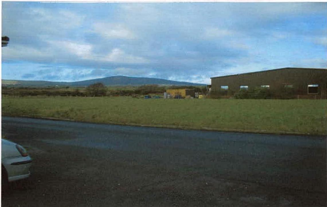 A photograph showing a large, dark commercial building situated next to a grassy field with hills in the background.