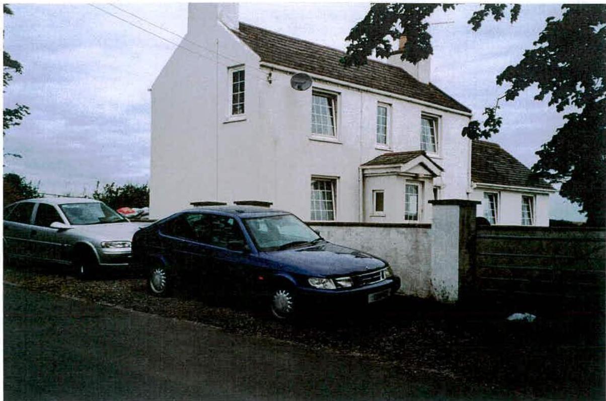 A photograph showing the front elevation of a white two-story detached house with cars parked on a gravel driveway.