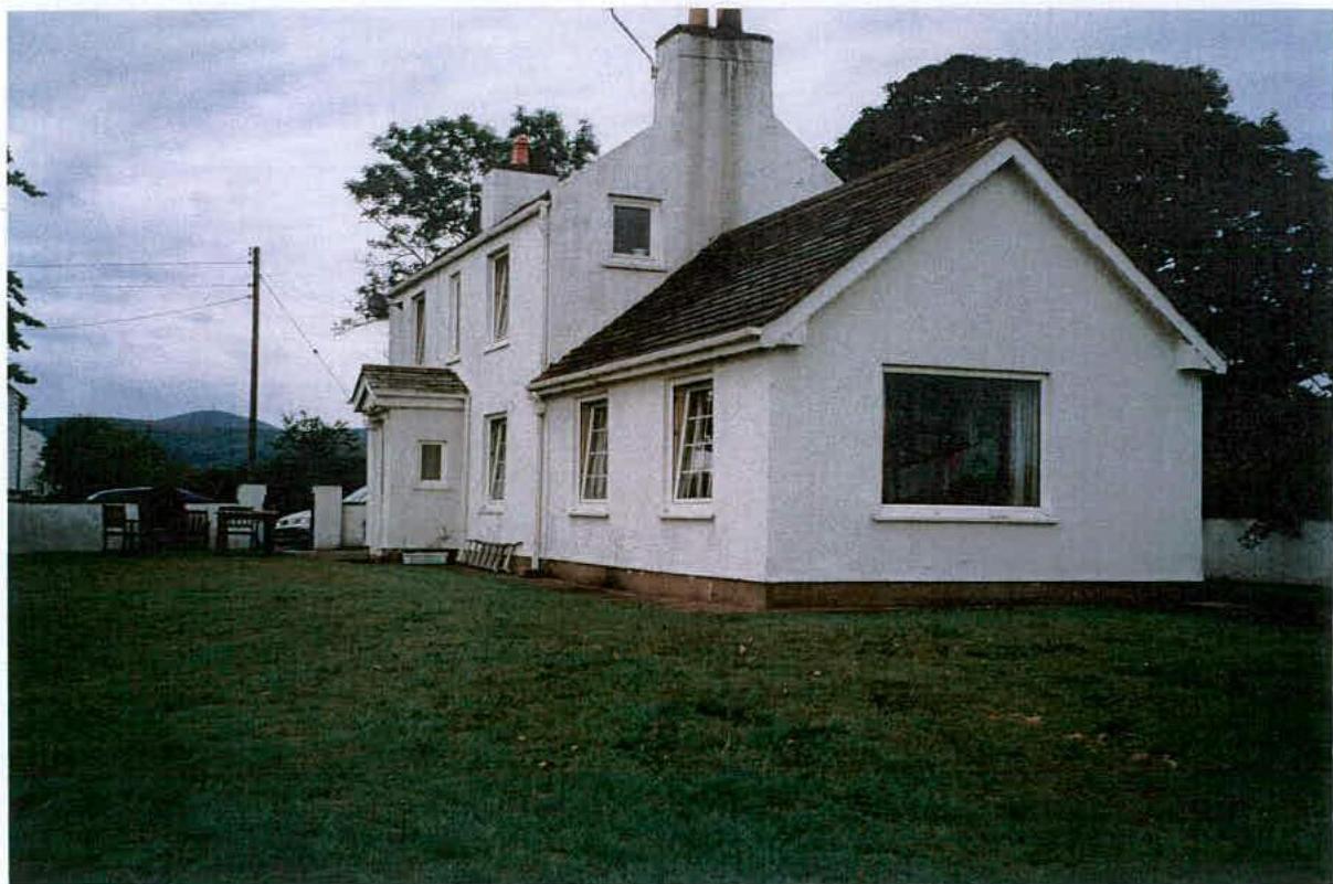 A photograph showing a white, two-story detached house with a pitched roof situated on a grassy lawn with trees in the background.