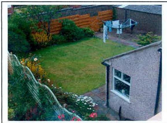 A photograph showing the rear garden of a property with a lawn, wooden fence, and a clothes horse.
