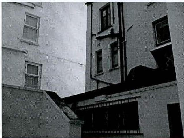 A grainy black and white photograph showing the exterior elevation of a multi-story building, likely terraced, with a lower ground floor section.