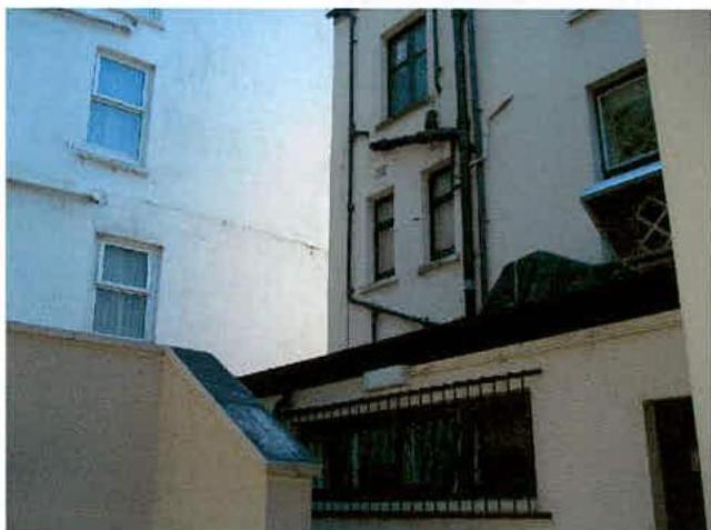 A photograph showing the exterior rear or side elevation of a white multi-story building with visible windows and downpipes.