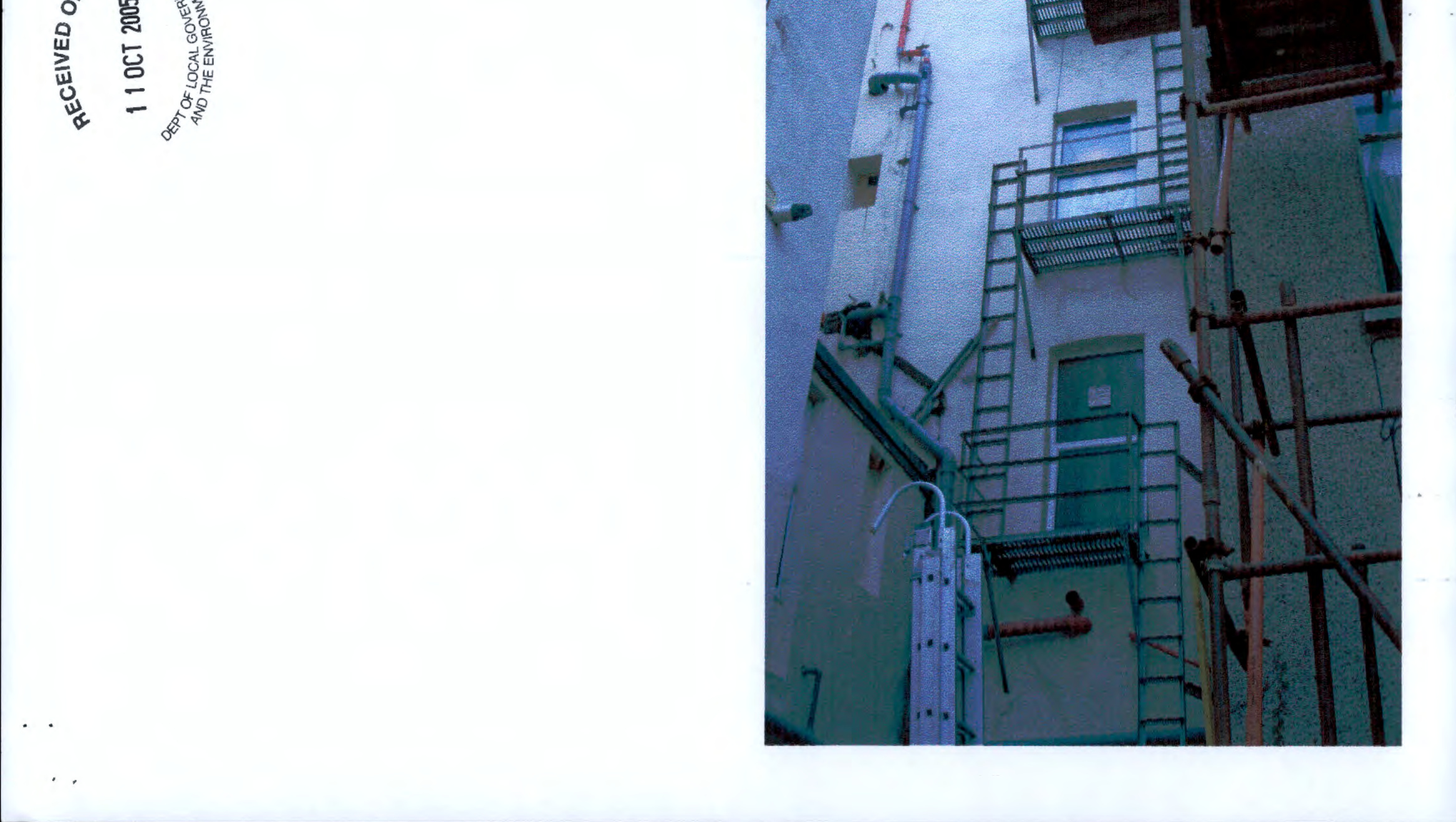 A scanned document page featuring a received stamp on the left and a photograph of a building exterior with external metal stairs and scaffolding on the right.