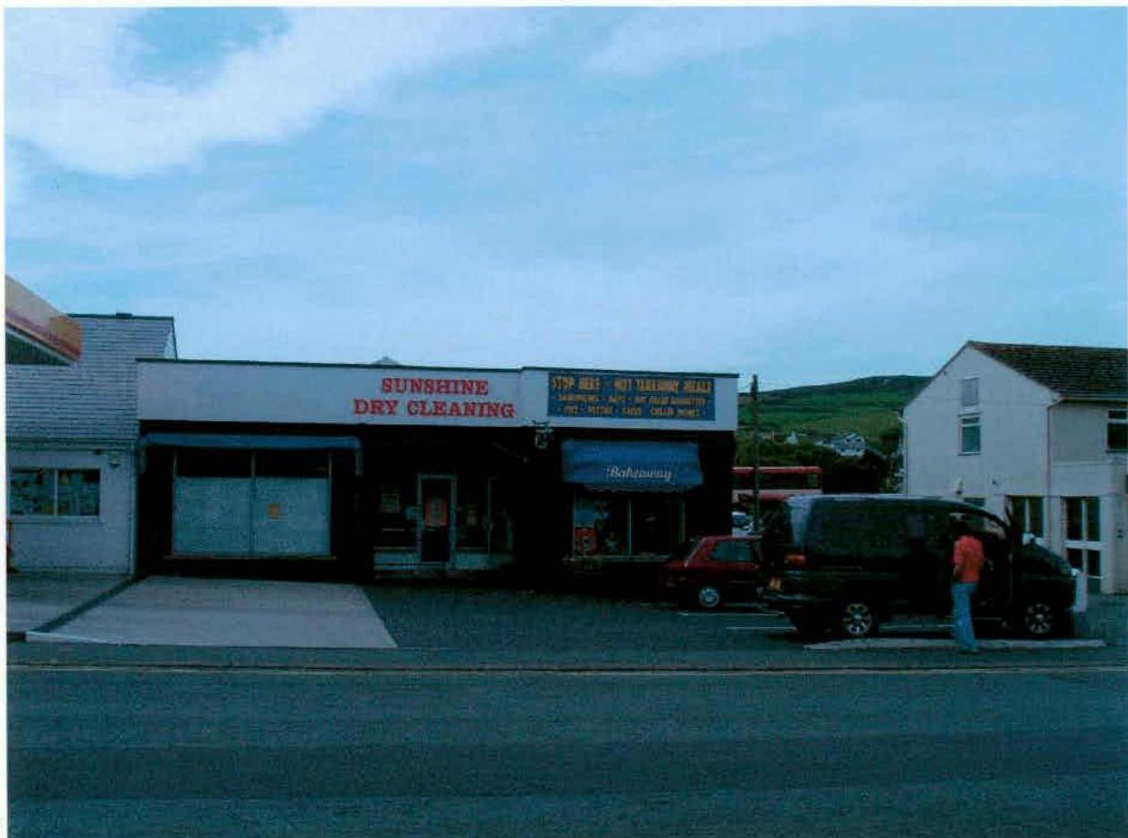 A street-level photograph of a commercial building featuring signs for 'Sunshine Dry Cleaning' and a hot food takeaway, with a black van parked in front.