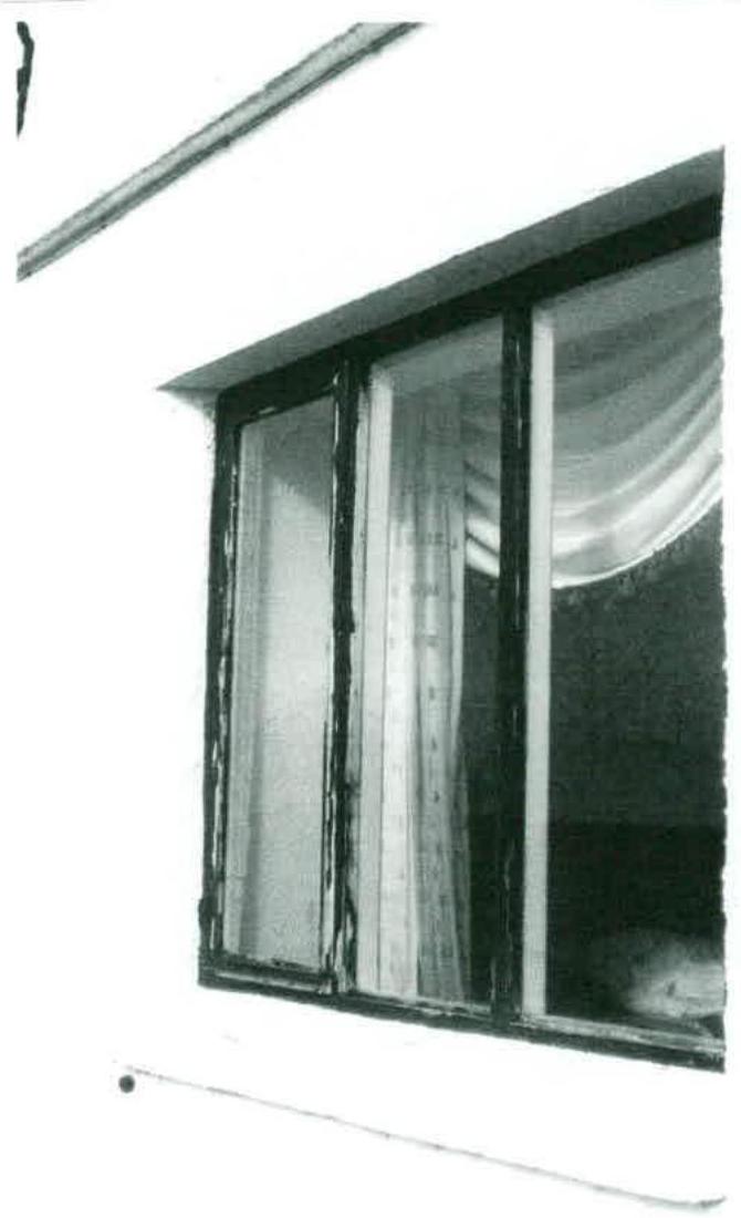 A grainy black and white photograph showing a close-up of a multi-pane window on the exterior wall of a building, with curtains visible inside.