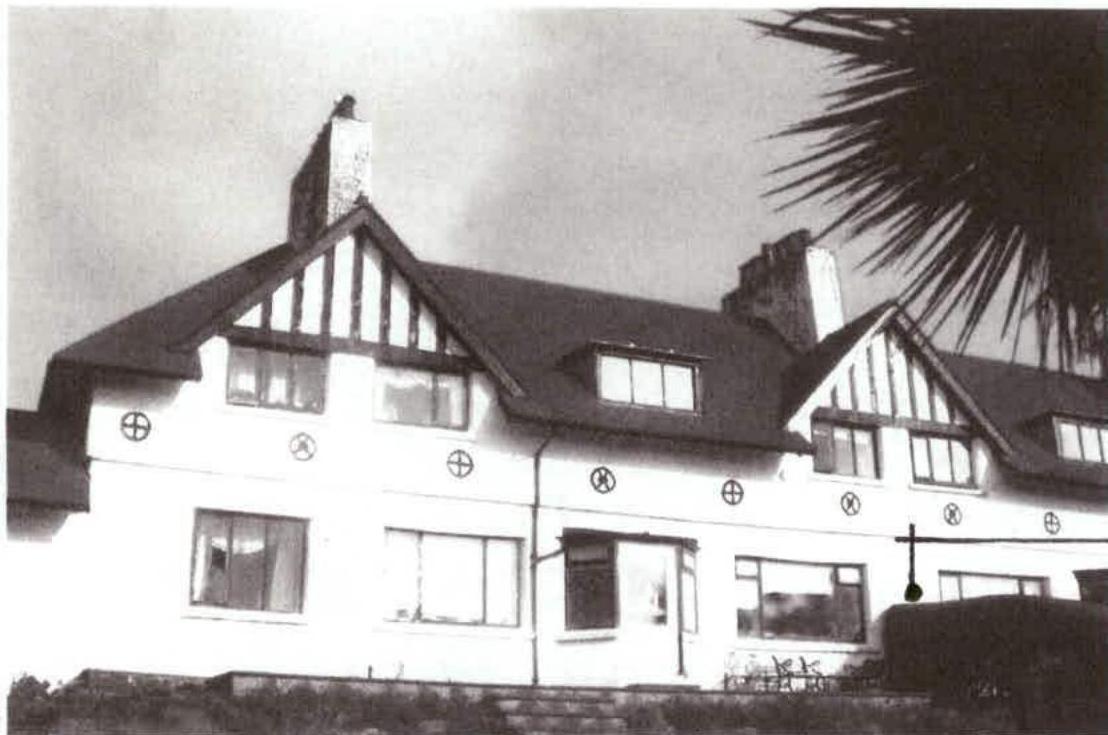 A black and white photograph showing the exterior elevation of a large house with distinctive gables, half-timbering details, and circular wall motifs.