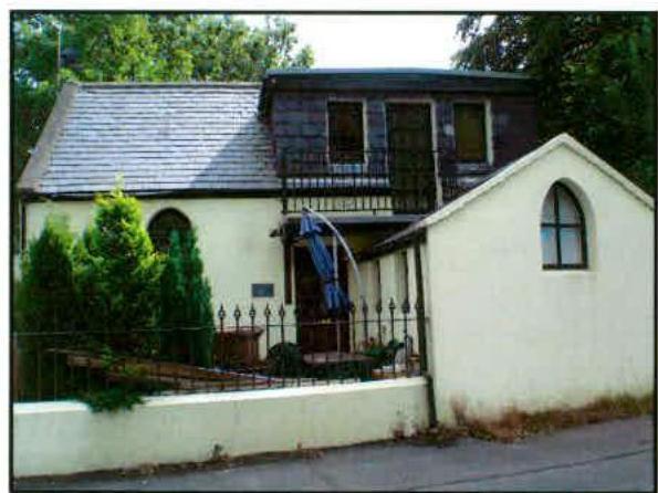A photograph showing the front elevation of a two-story residential property with a balcony and an attached single-story structure.