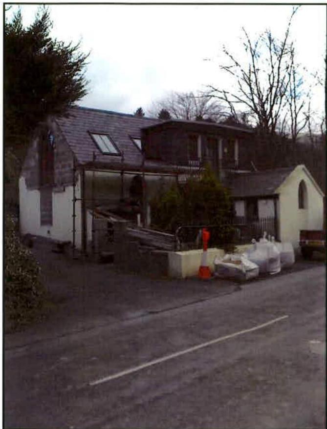 A photograph showing a white cottage-style building with a large glass sunroom extension under construction, featuring scaffolding and building materials.