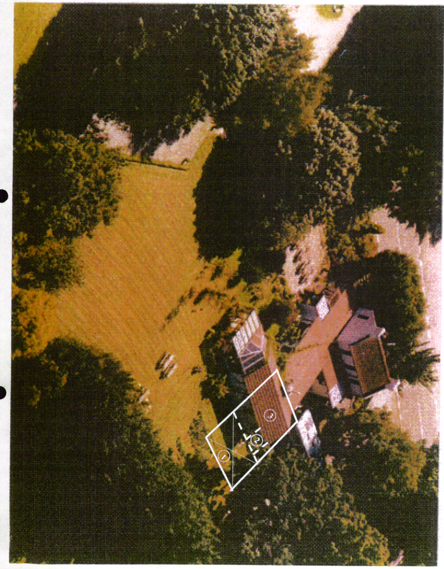 An aerial photograph of a rural property featuring trees and fields, with a white line drawing overlaid to indicate a site boundary or proposed development area.