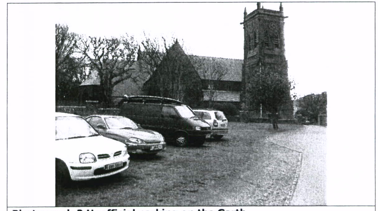 A black and white photograph showing several cars parked on a grassy area in front of a large stone building with a tower.
