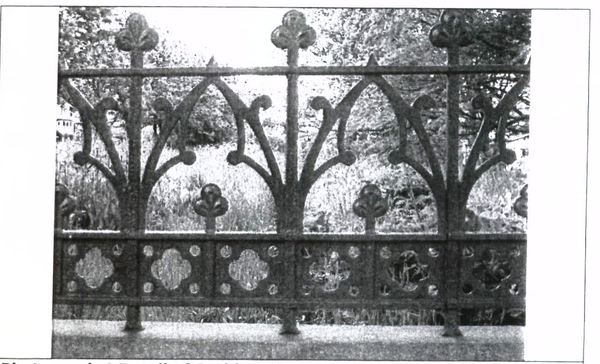 A black and white photograph showing an ornate, Gothic-style metal fence or railing with trefoil designs and decorative lower panels.