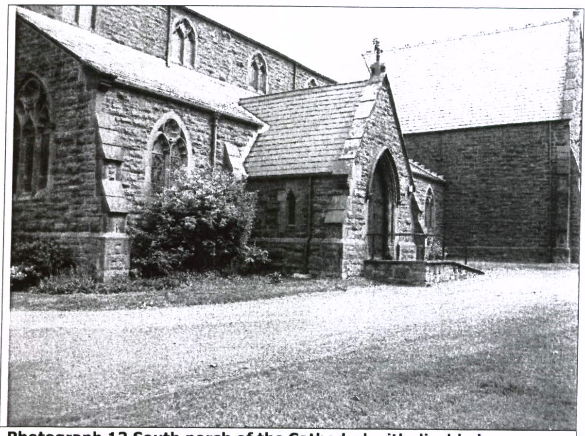 A black and white photograph showing the exterior of a stone church or cathedral, specifically focusing on a south porch structure with Gothic-style windows.