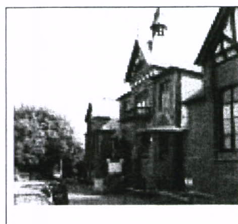 A grainy black and white photograph showing the exterior of a residential building featuring a turret and gabled roofline.