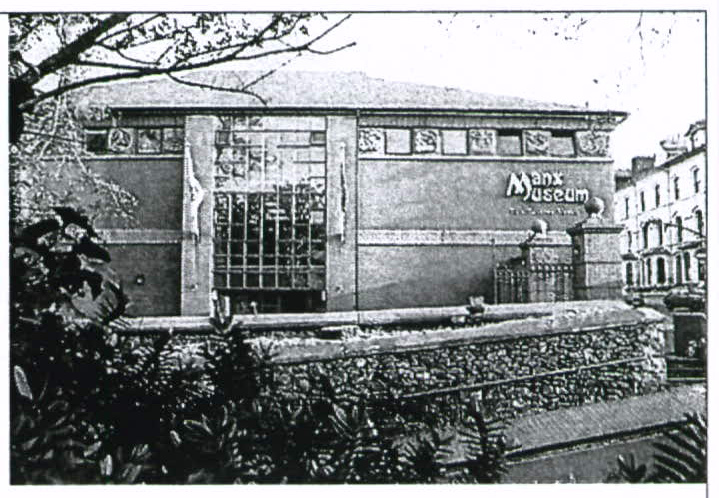 A black and white photograph showing the exterior of the Manx Museum building with a stone wall and foliage in the foreground.