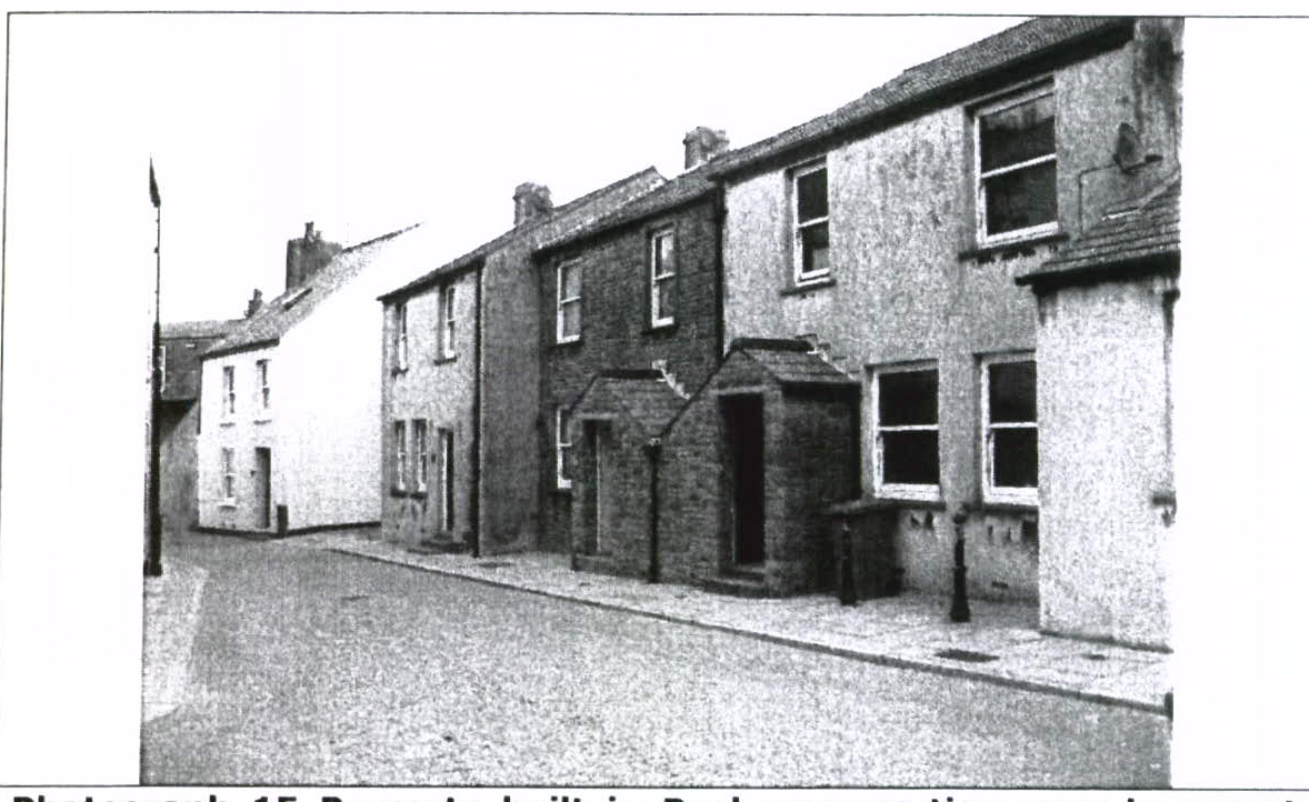 A black and white photograph showing a row of traditional terraced residential buildings along a street.