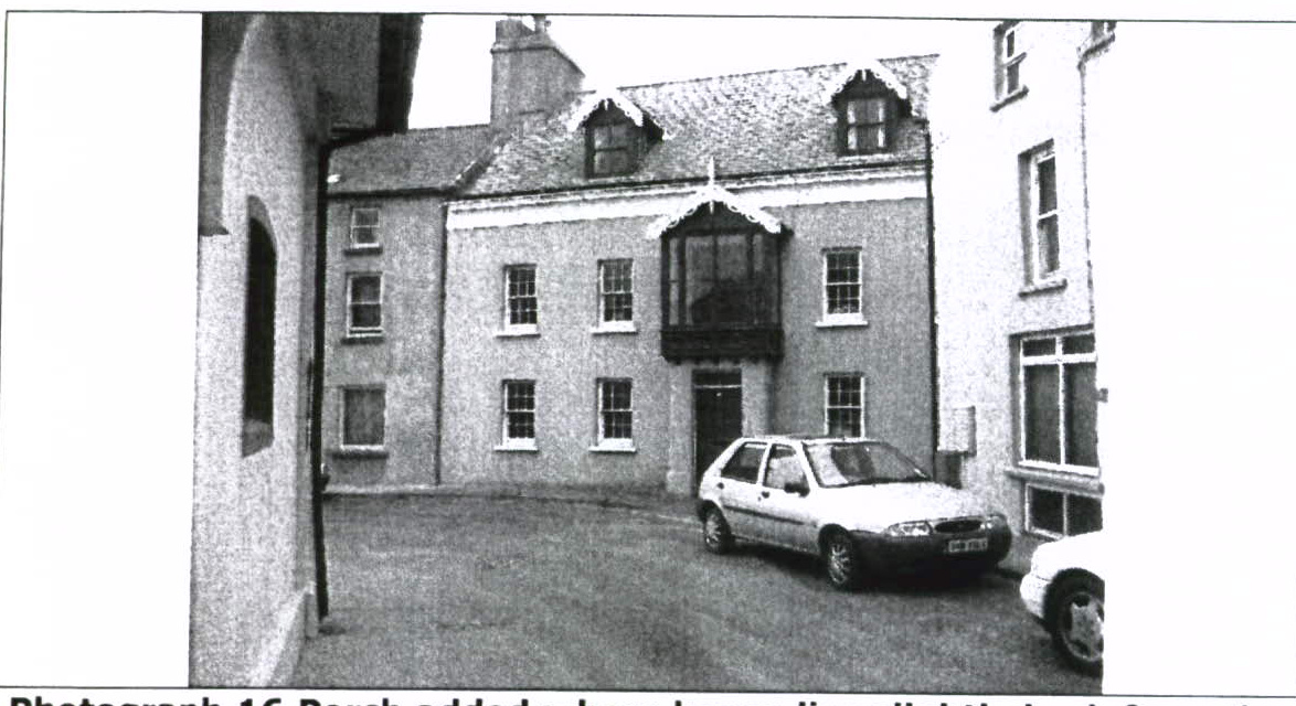 A grainy black and white photograph showing the front elevation of a two-story residential building with a car parked in the driveway.