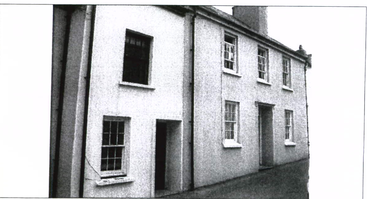 A grainy black and white photograph showing the side elevation of a two-story building with a mix of window styles and textures.