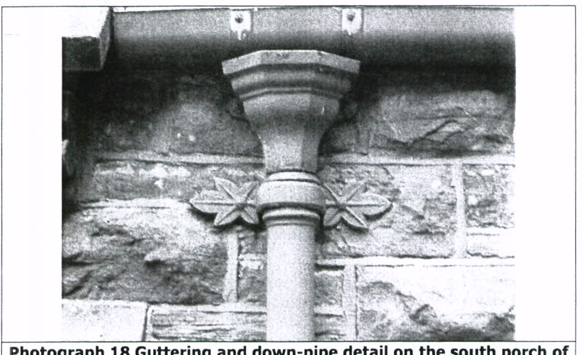 A black and white photograph showing a close-up detail of a stone wall with a decorative downpipe bracket and guttering.