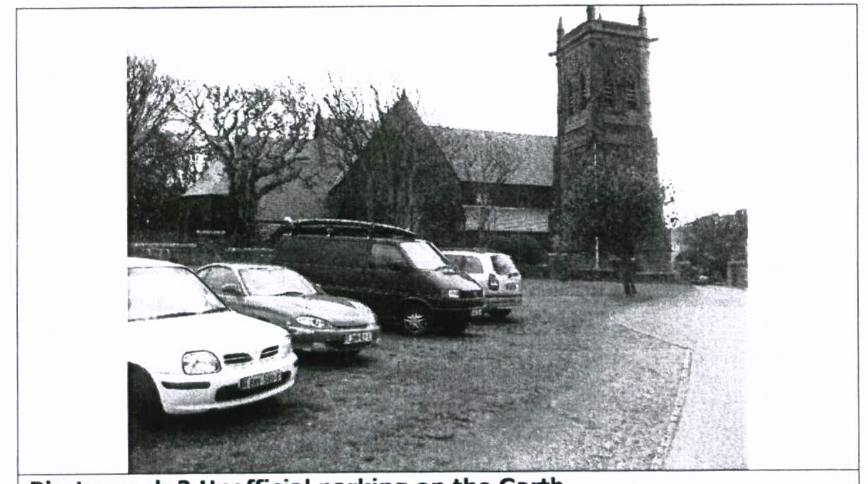 A black and white photograph showing several cars parked on a grassy area in front of a large stone building with a prominent tower.
