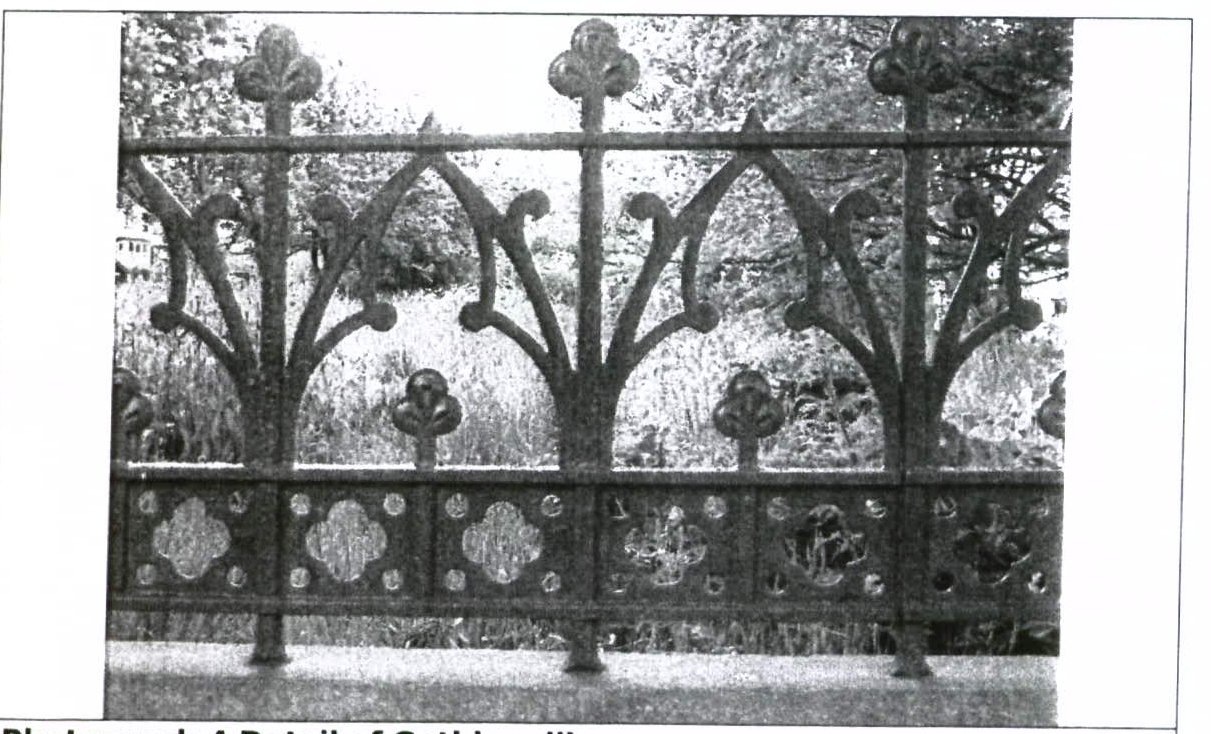 A black and white photograph showing a close-up detail of an ornate, Gothic-style metal fence or railing with trefoil motifs.
