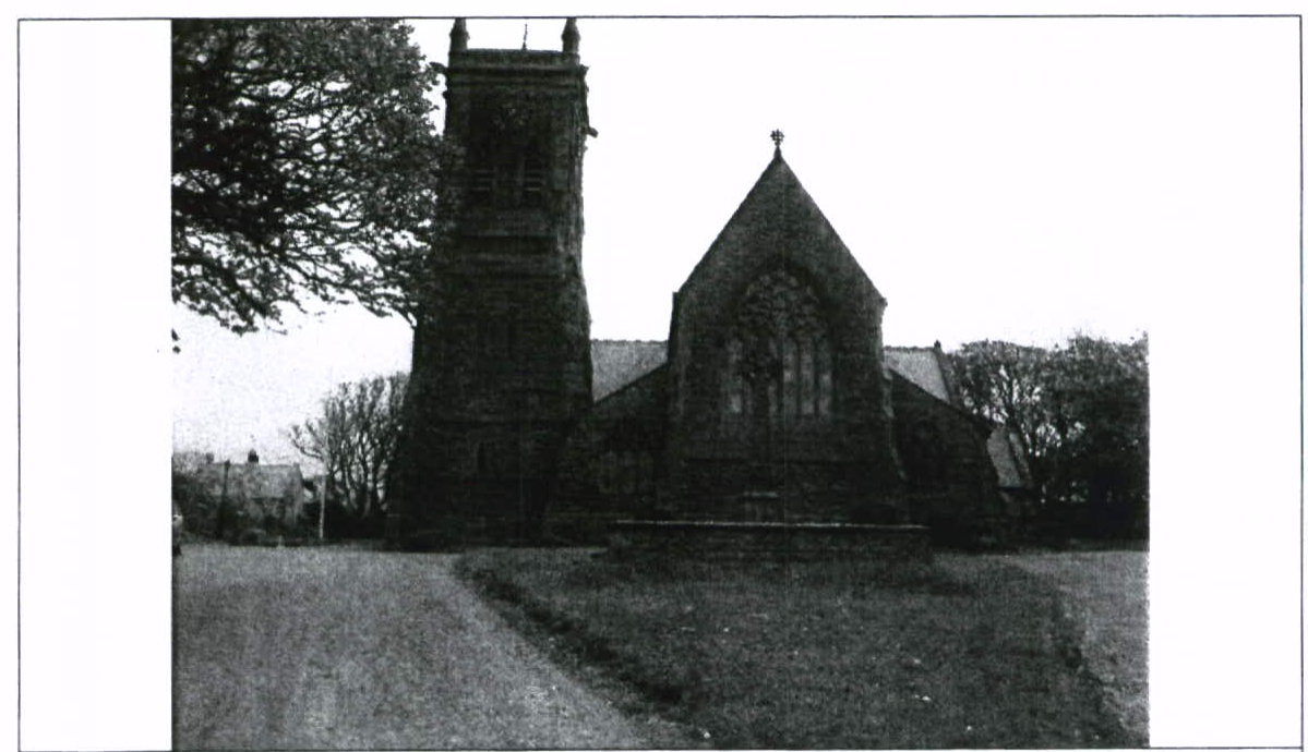 A black and white photograph showing a stone church or chapel with a tower and cross, situated in a grassy area.