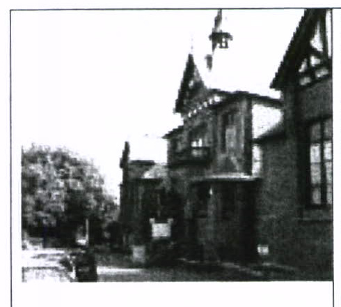 A grainy black and white photograph showing the exterior of a substantial building with gabled roofs and timber detailing.