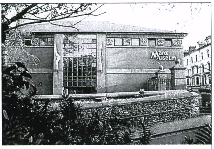 A black and white photograph showing the exterior facade of the Manx Museum building with a stone wall and vegetation in the foreground.