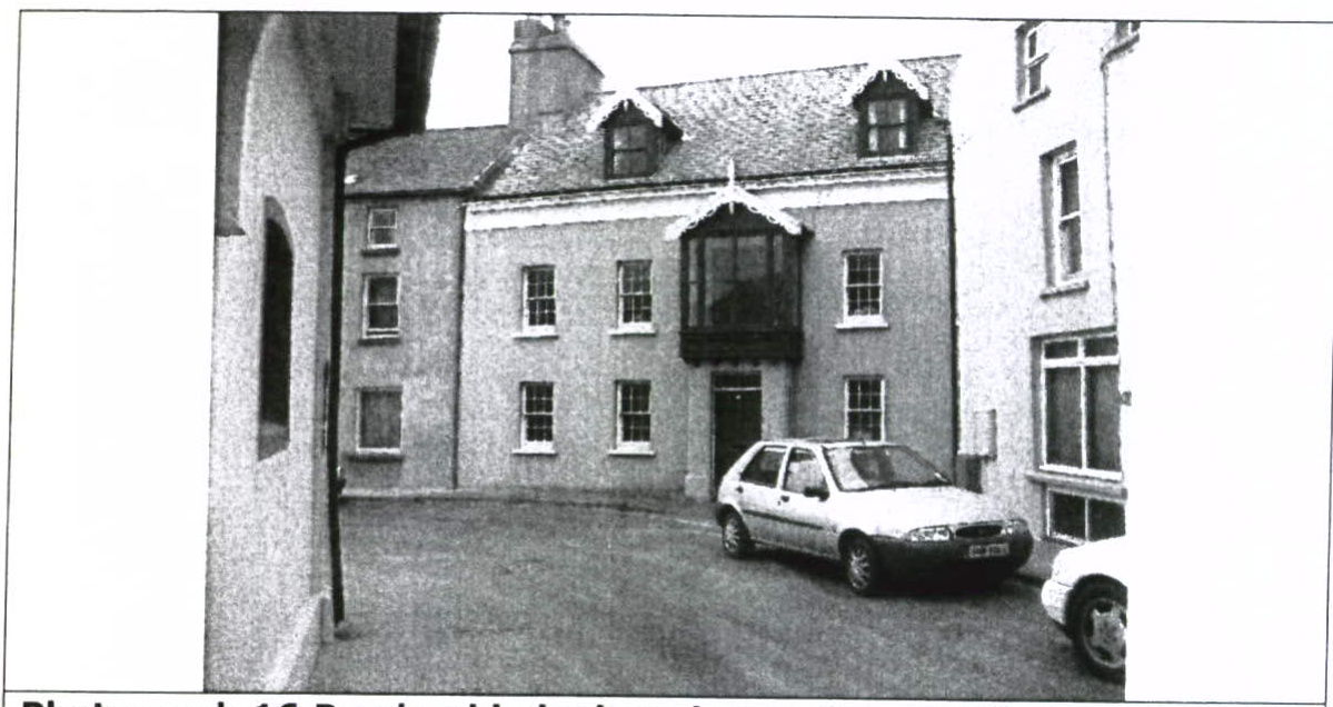 A black and white photograph showing the front elevation of a two-story terraced building with a car parked in the driveway.