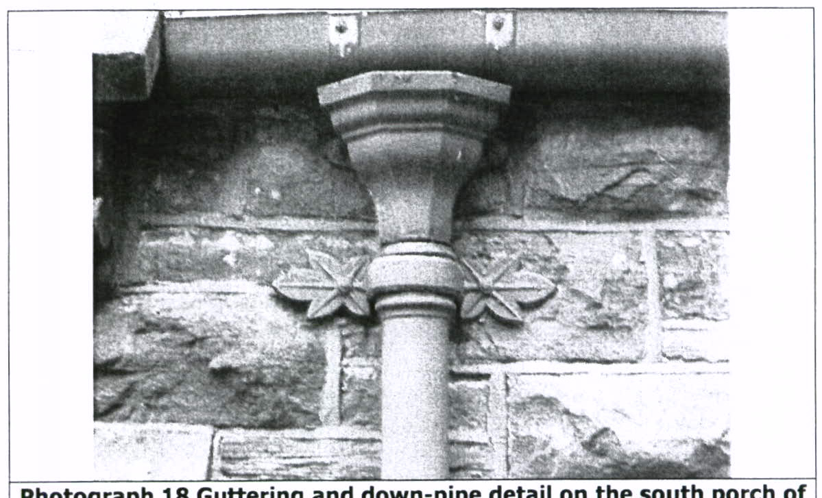 A black and white close-up photograph showing a stone downpipe with decorative capital and leaf details against a rough stone wall.
