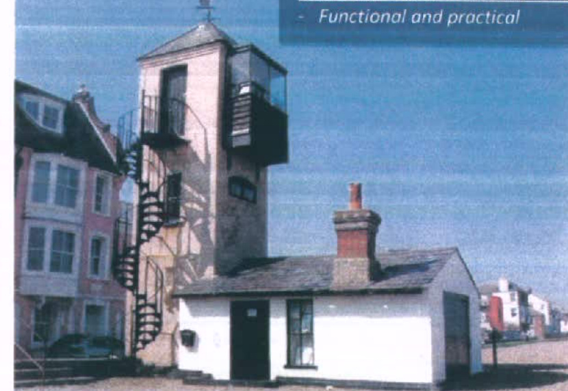 A photograph showing a street scene featuring a distinctive building with a tall tower structure, spiral staircase, and glass upper section, alongside a small white outbuilding.