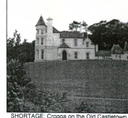 A grainy black and white photograph showing a large white house with a turret situated on a grassy slope with trees in the background.