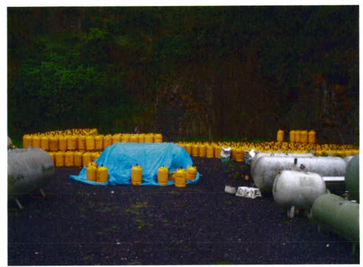 A photograph showing an outdoor fuel storage area with rows of yellow jerry cans and large white cylindrical tanks.