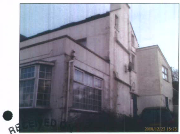 A low-resolution photograph showing the exterior facade of a two-story building with large windows and a chimney stack, likely a former hotel.