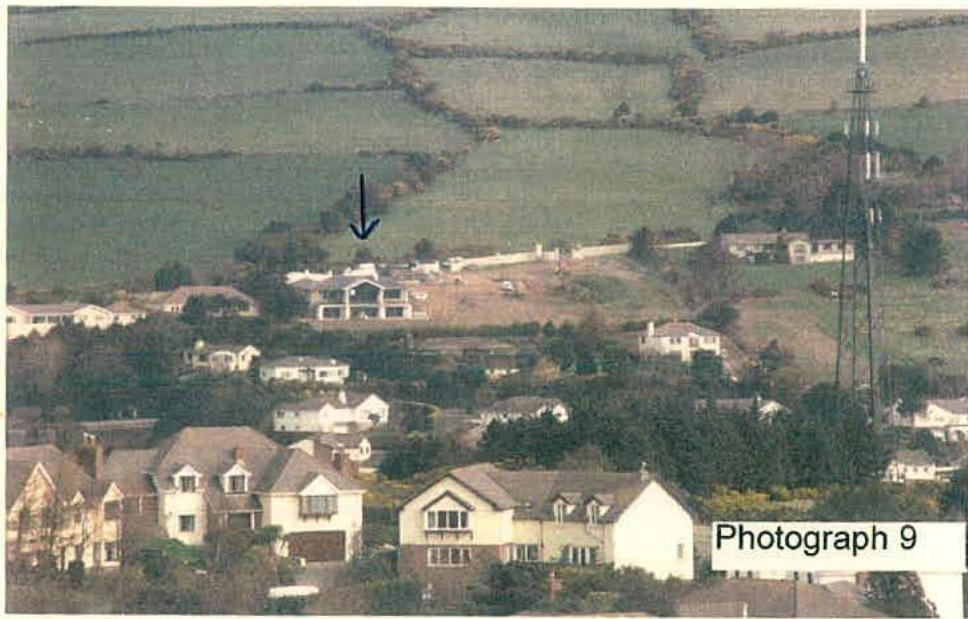 A distant photograph of a hillside residential area with a black arrow pointing to a white building, labeled 'Photograph 9' in the corner.