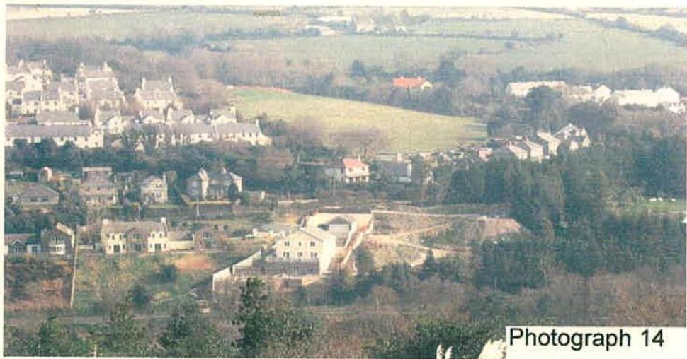 A wide-angle photograph showing a new house construction site in the foreground with surrounding residential houses and fields in the background.