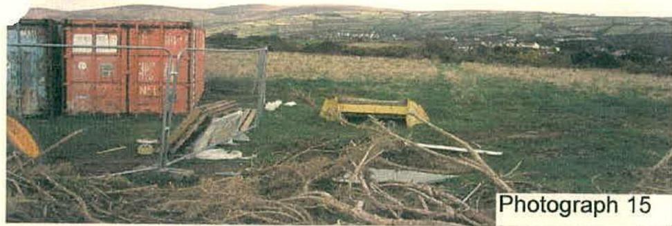 A photograph of a rural site showing shipping containers, agricultural machinery, and debris on a grassy field.
