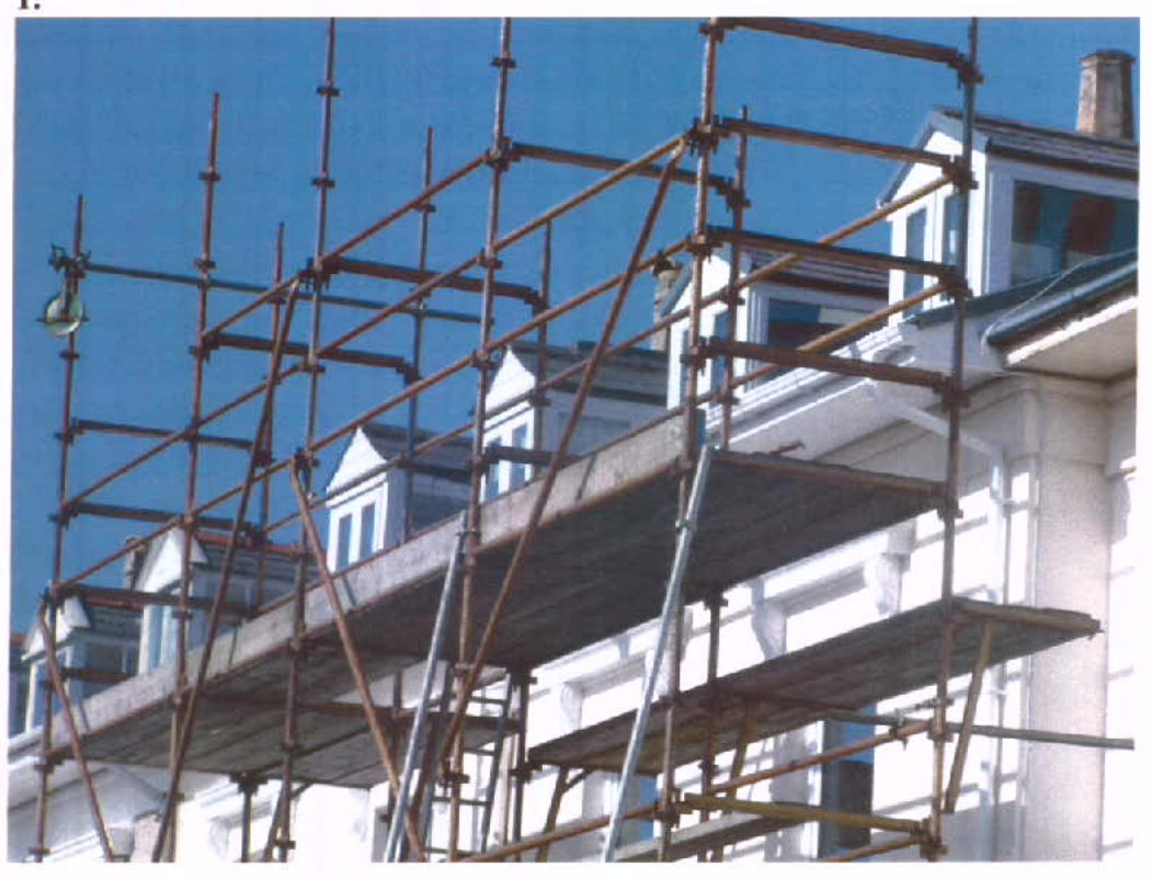 A photograph showing a white residential building with new dormer windows installed, covered in scaffolding against a blue sky.
