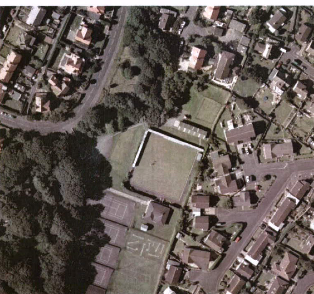 An aerial view showing a sports field, tennis courts, and surrounding residential properties in a village setting.