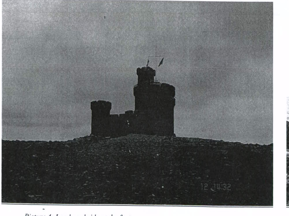 A black and white photograph showing the silhouette of a castle-like tower structure on a hill against a cloudy sky.