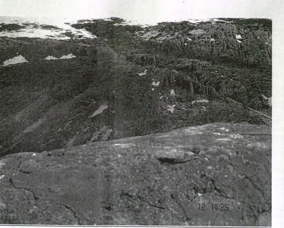 A black and white photograph depicting a rugged, rocky landscape with patches of snow or light ground, likely showing a coastal cliff or hillside terrain.