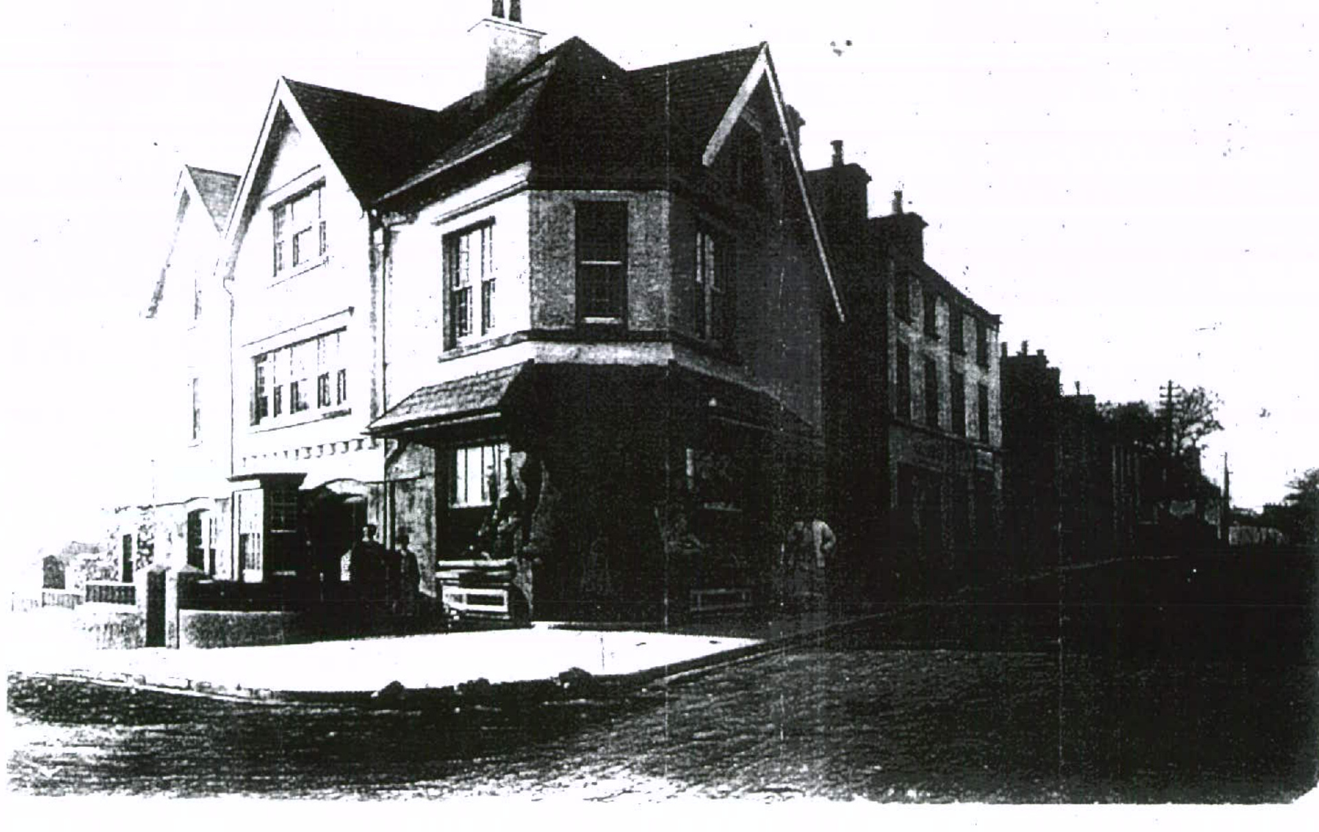A black and white historical photograph showing a corner commercial building with a shop front and canopy.