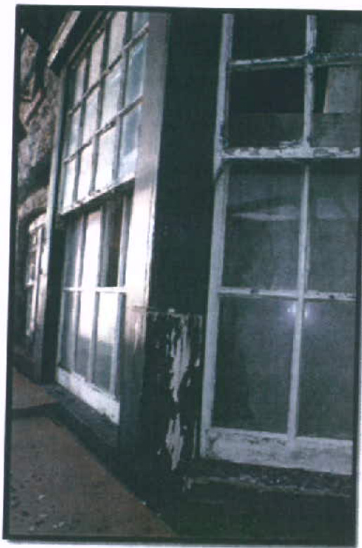 A photograph showing the exterior facade of a building featuring large, multi-paned sash windows with visible wear and peeling paint.