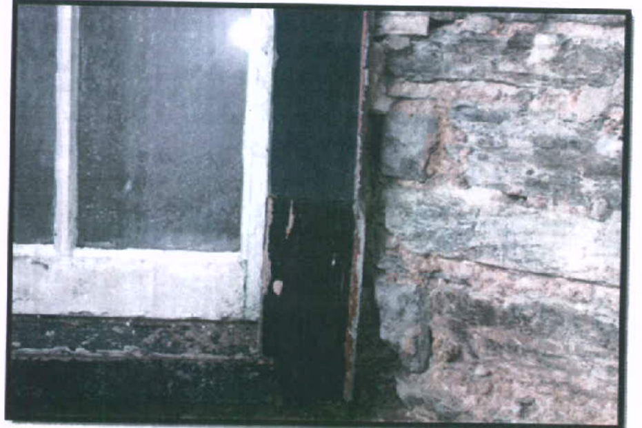 A close-up photograph showing a white window frame adjacent to a rough stone wall.